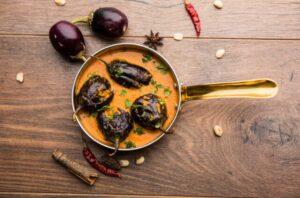 A pot of roasted eggplant curry with some curry ingredients scattered on the table