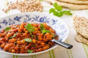 Chickpea curry in a bowl with a few pieces of naan, chickpea, and cilantro in the background