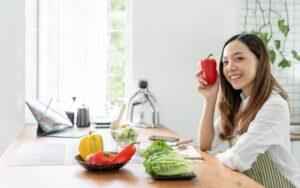A woman posing with different types of vegetables in a kitchen
