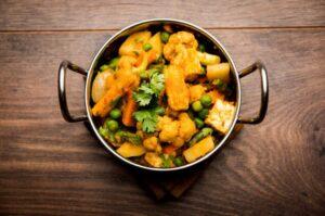 Mixed vegetable curry in a steel pot on top of a wooden table