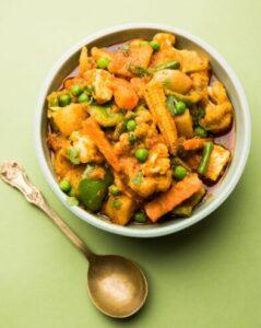 A bowl of curry with mixed vegetables topping against a green background
