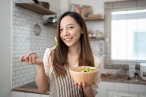 A woman posing with a bowl of salad in a kitchen